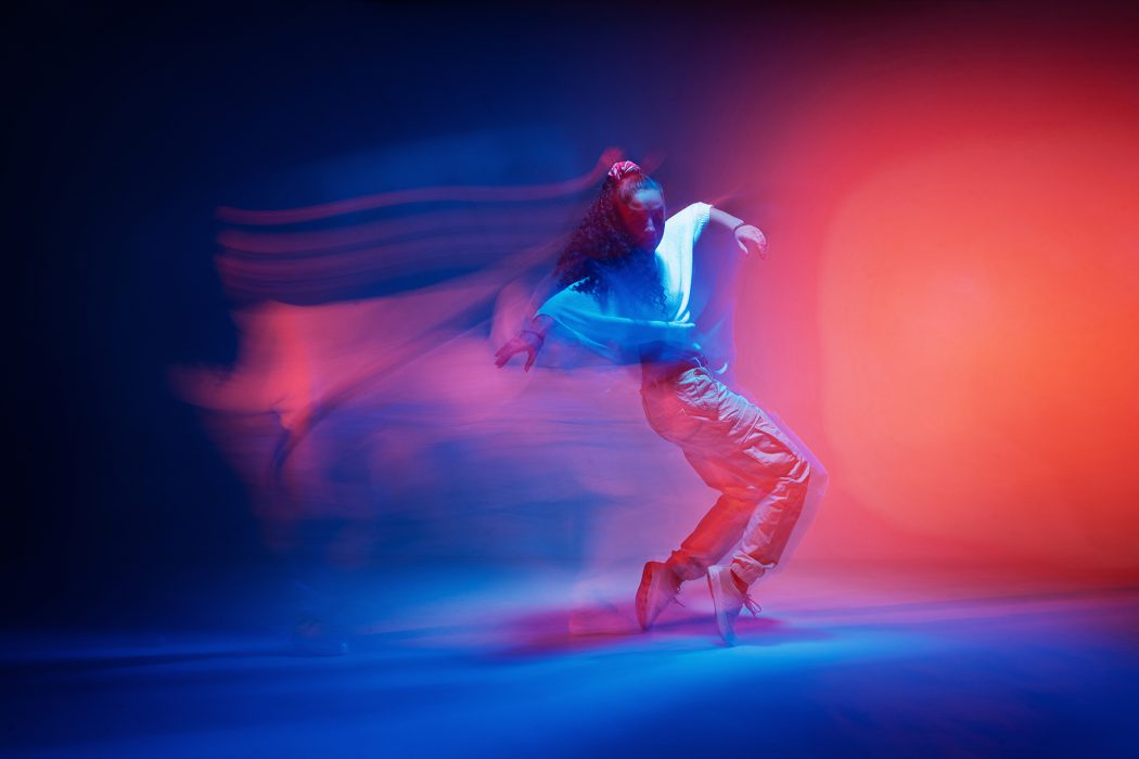 Dancing female standing on tiptoe in colourful neon studio light. Long exposure. Contemporary hip hop dance