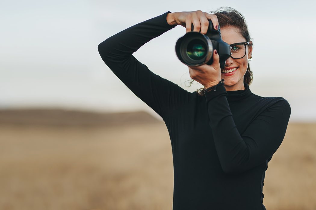 Professional female photographer with dslr camera photographing outdoors. Young woman with camera taking pictures.