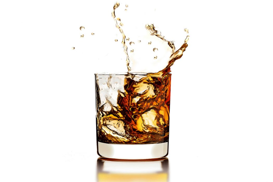 Whisky splashing out of the glass with ice cubes isolated on white with reflection